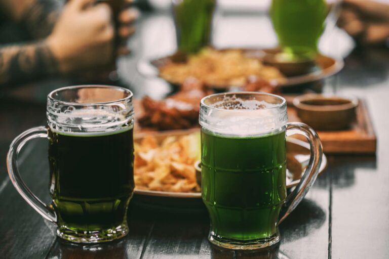 Mugs with green beer on table in pub and corned beef. Irish St. Patrick's Day.